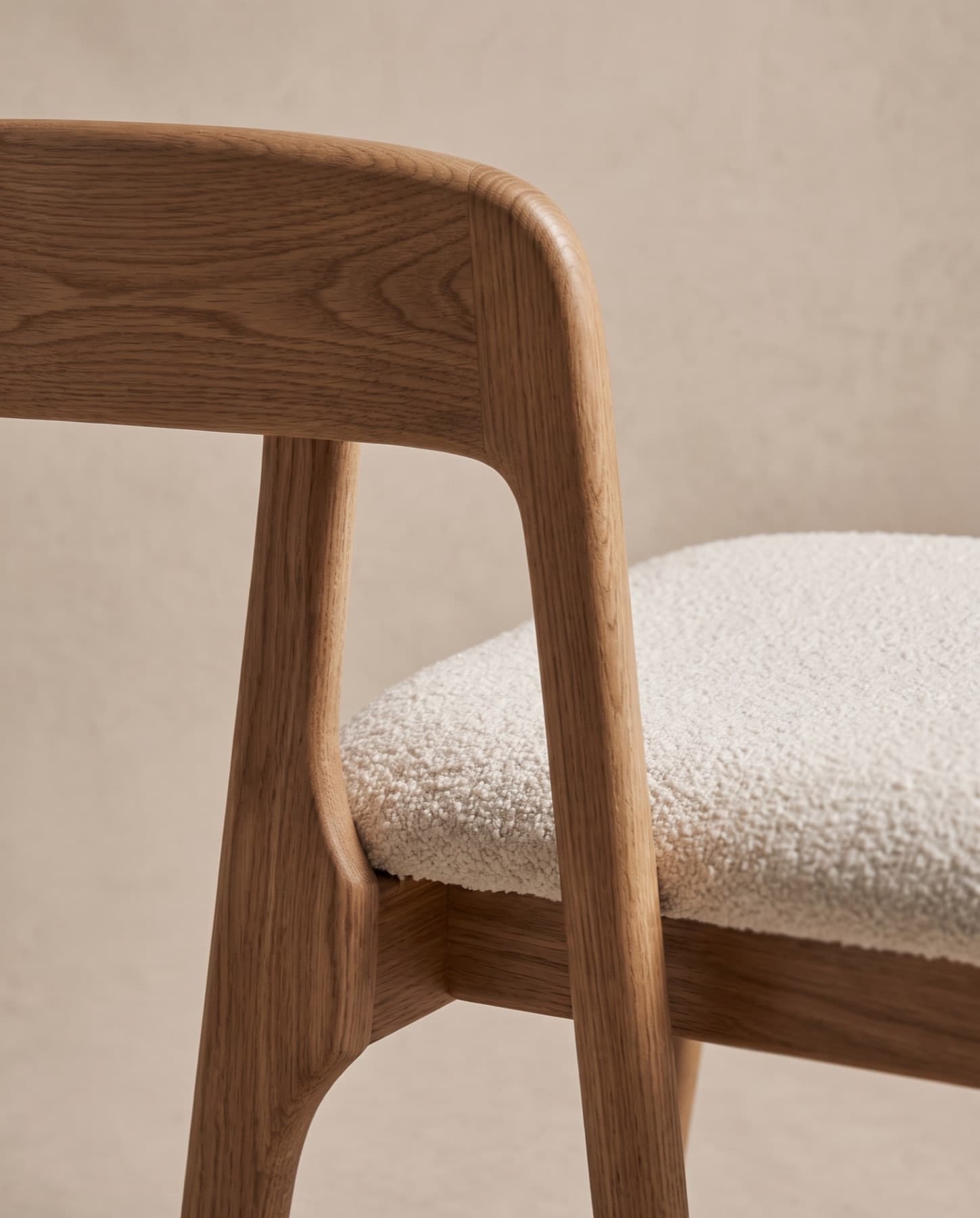 Close-up of the hand-finished joint where the oak back rail of the Arden chair meets the leg, above the bouclé seat