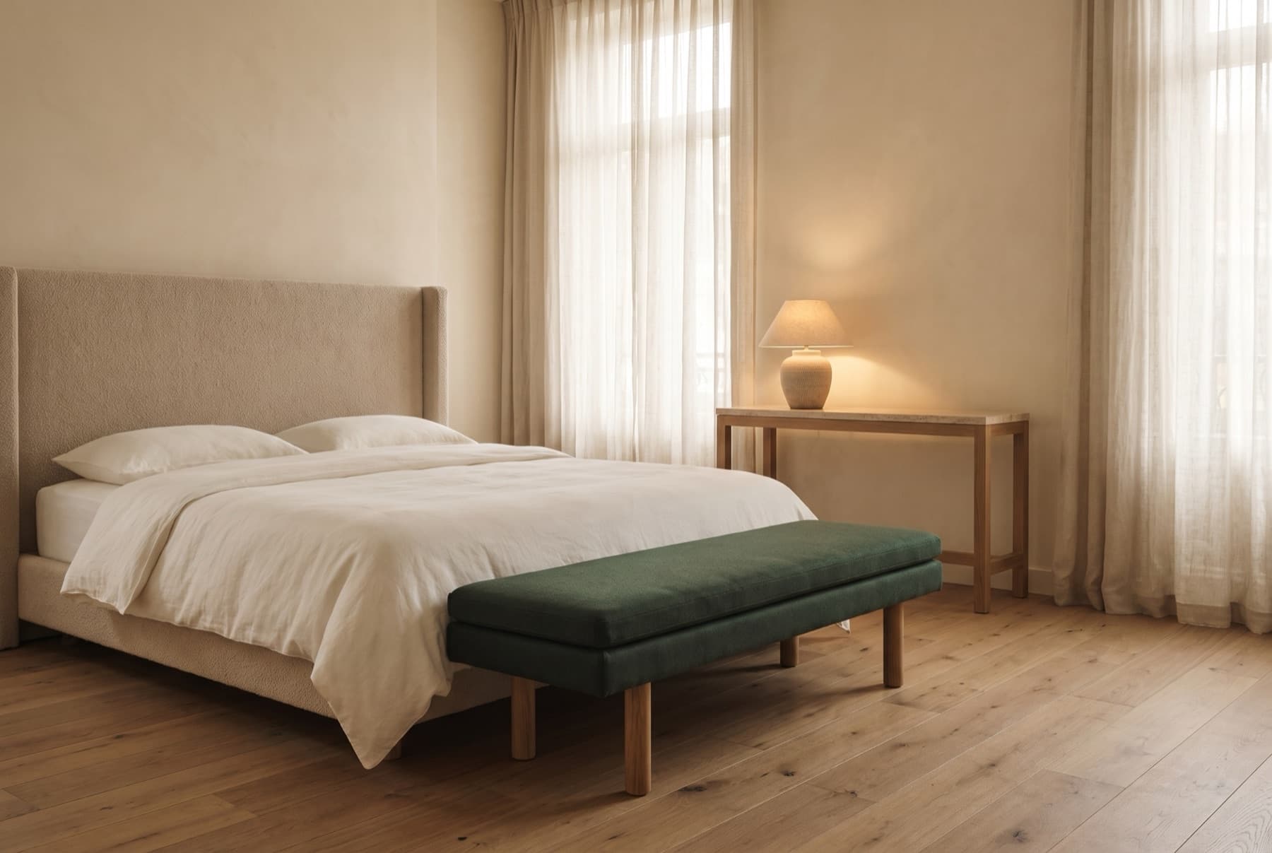 Hotel suite with a tall upholstered headboard, white bedding, a forest-green bench at the foot of the bed and a slim console