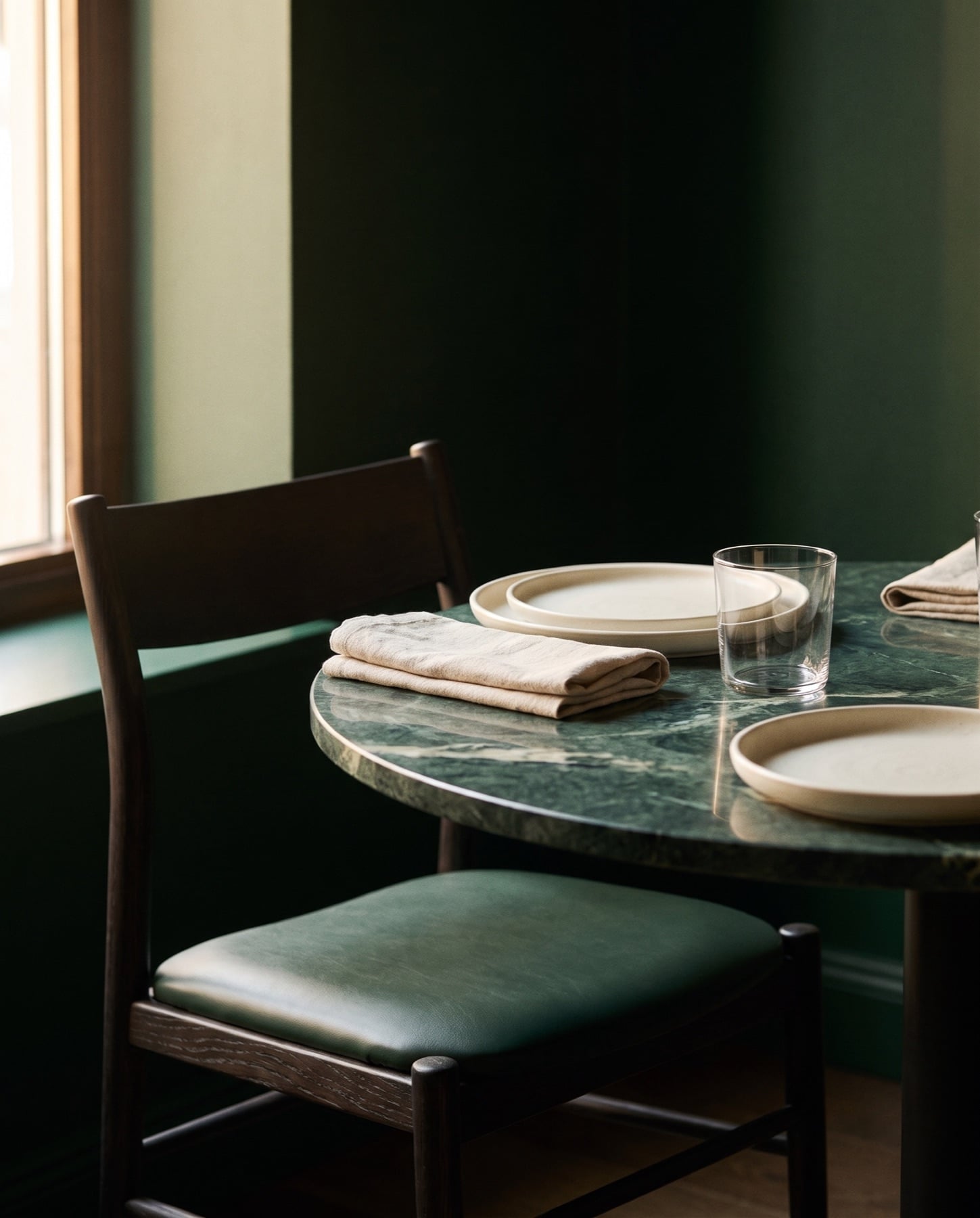 Dark stained dining chair with a green leather seat at a Verde Alpi marble table set with plates